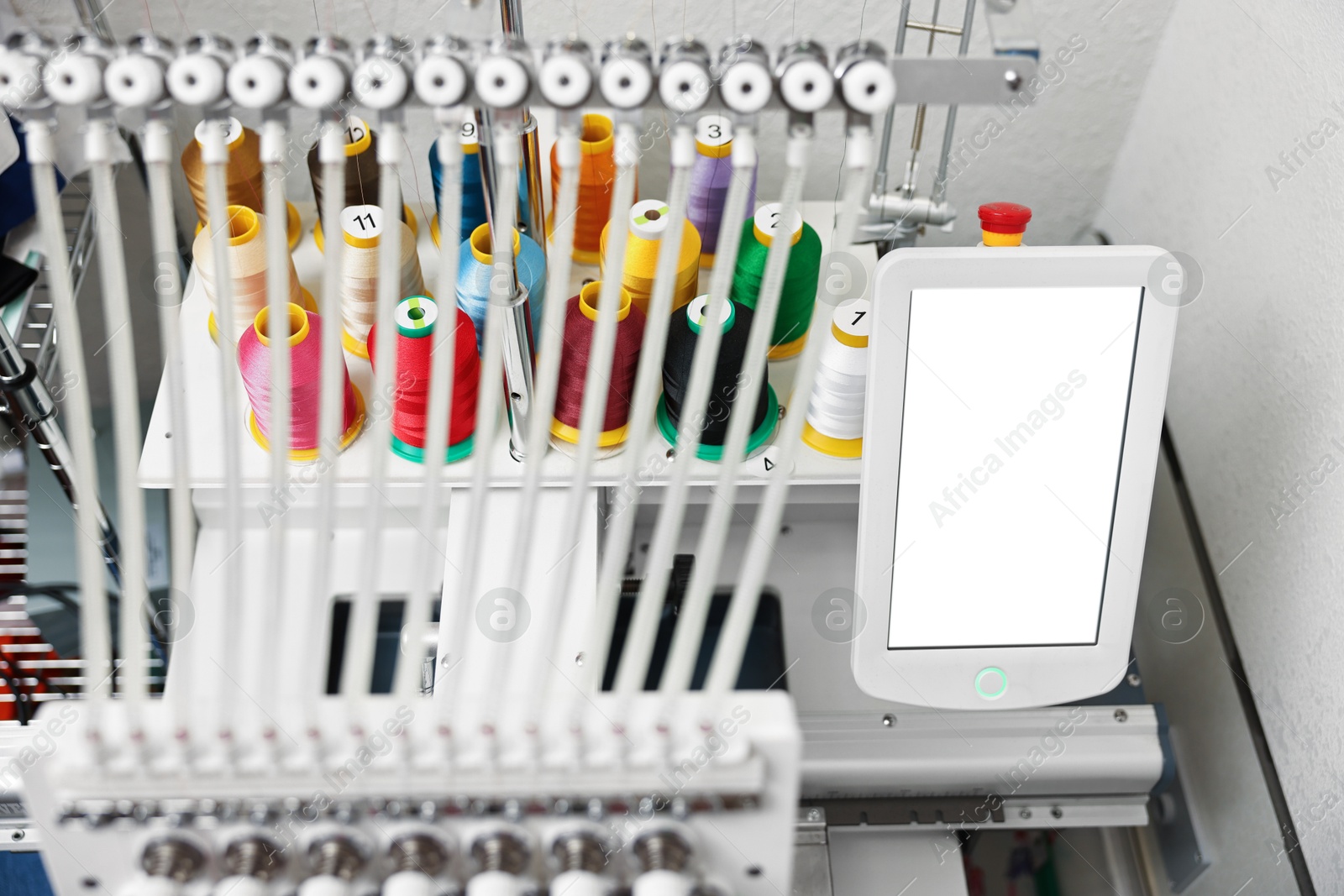 Photo of Modern embroidery machine with spools of thread indoors, closeup