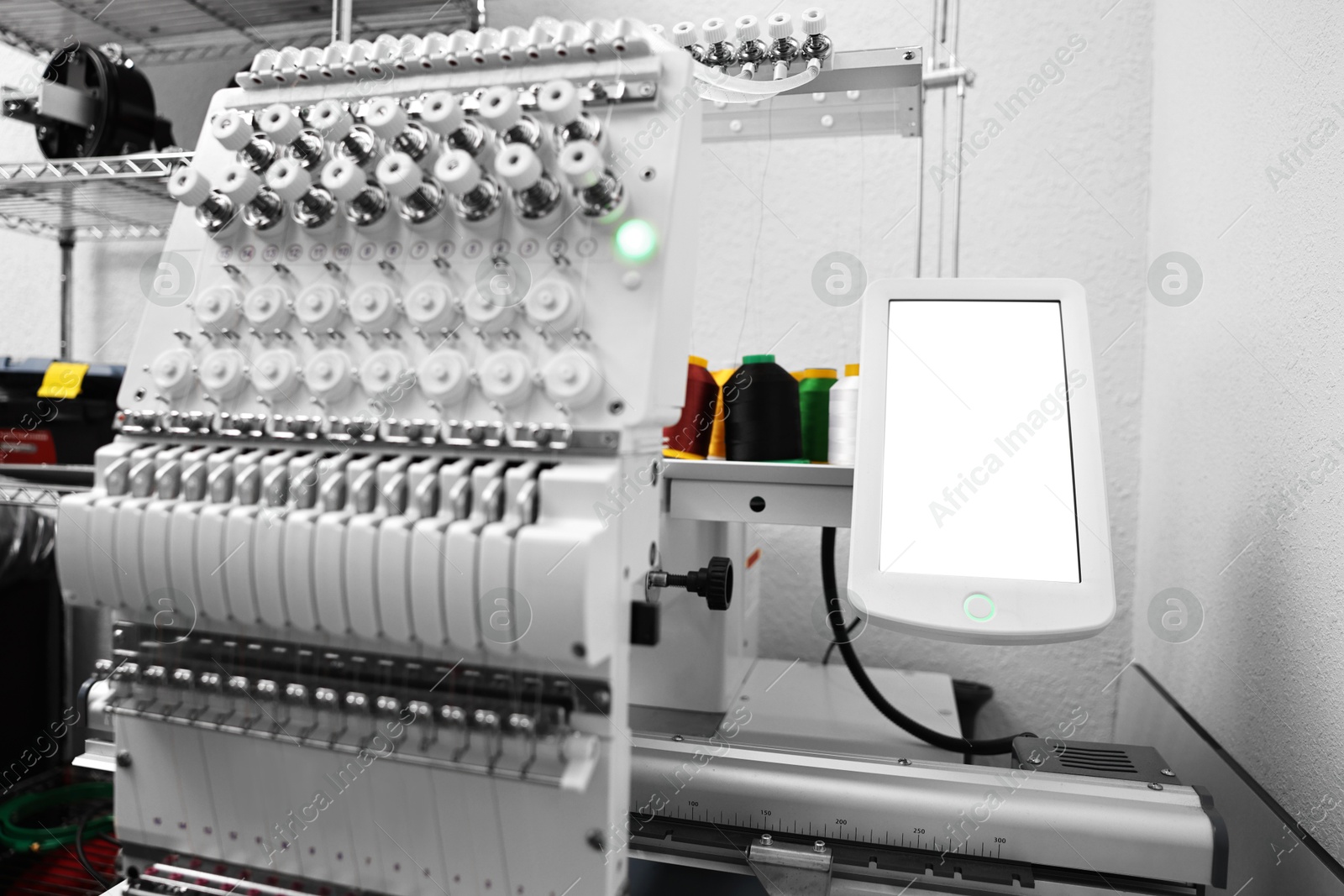 Photo of Modern embroidery machine with spools of thread indoors