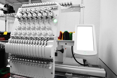 Photo of Modern embroidery machine with spools of thread indoors