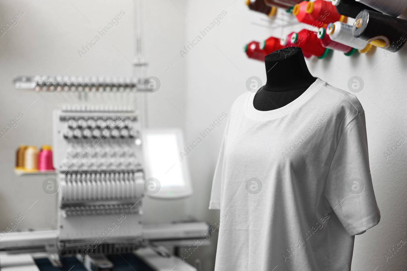 Photo of Mannequin with blank T-shirt for print and modern embroidery machine indoors, selective focus