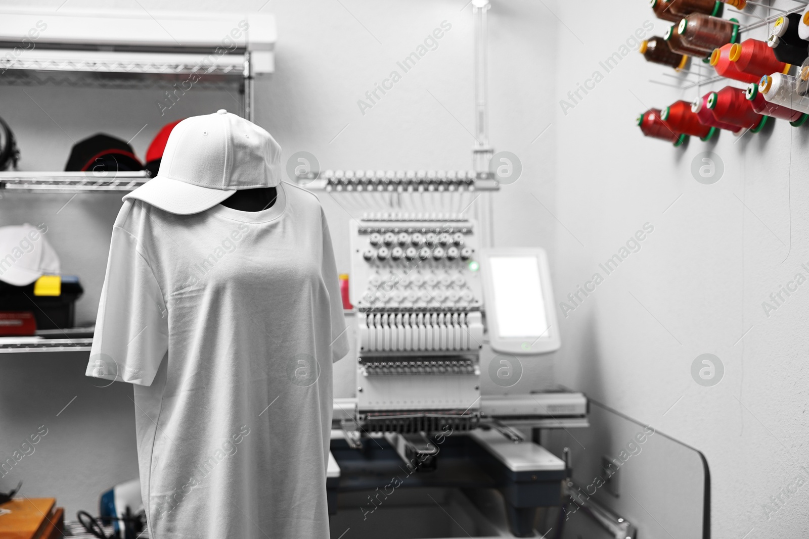 Photo of Mannequin with blank T-shirt for print, cap and modern embroidery machine indoors