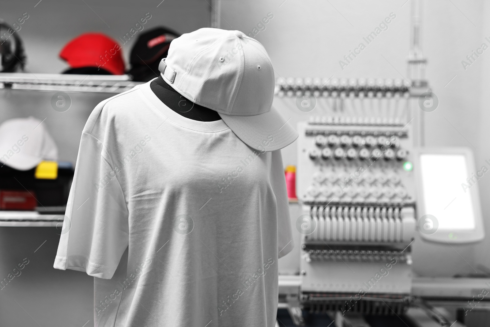 Photo of Mannequin with blank T-shirt for print, cap and modern embroidery machine indoors