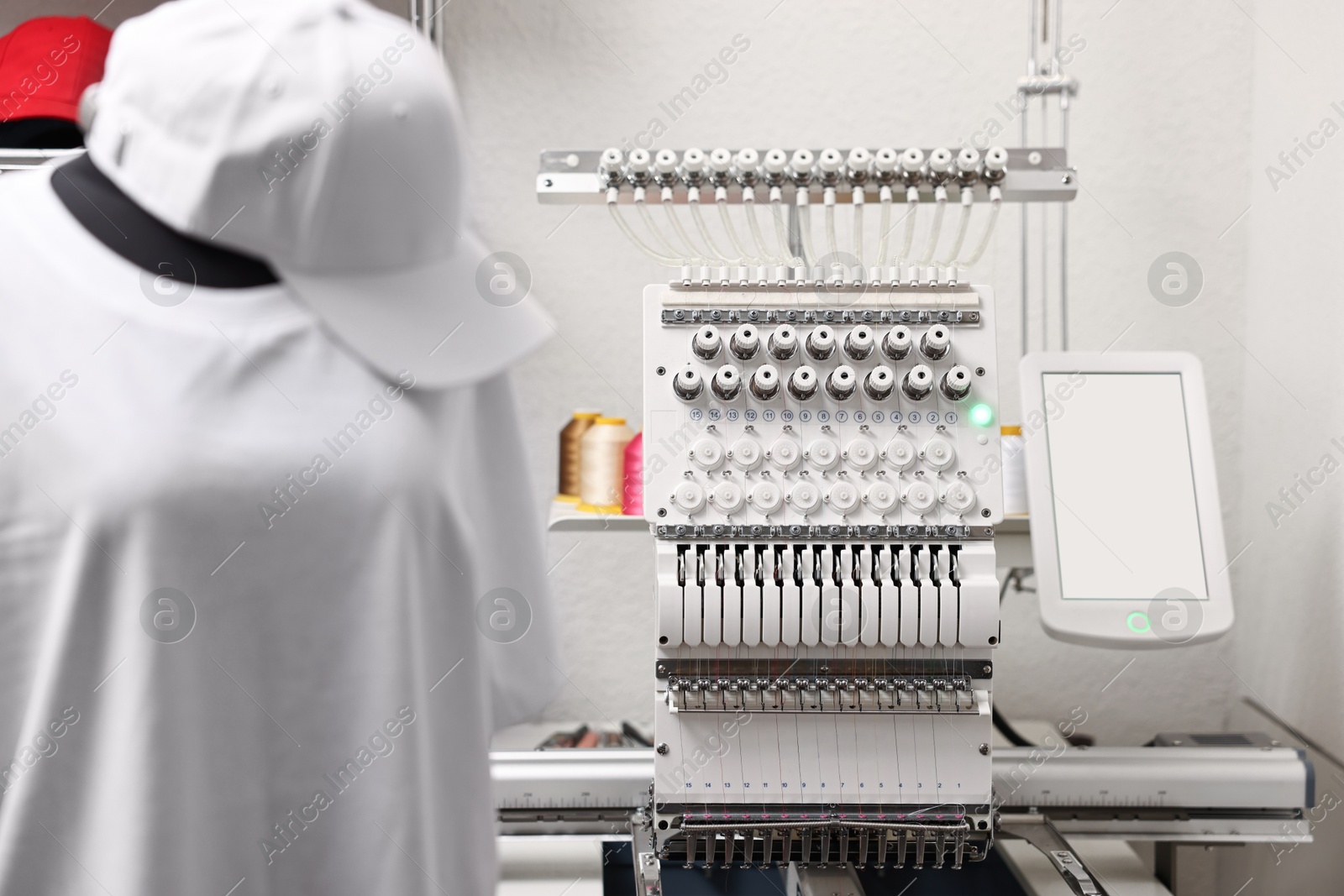 Photo of Mannequin with blank T-shirt for print, cap and modern embroidery machine indoors