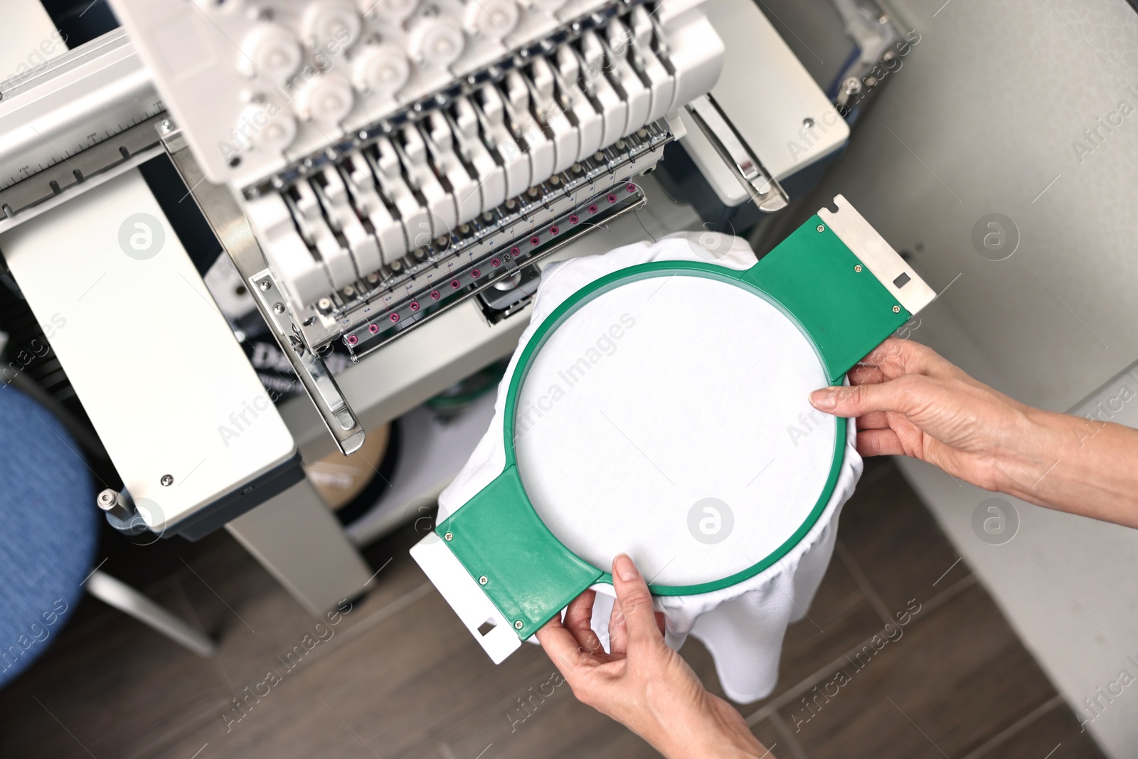 Photo of Woman using embroidery machine to make design on T-shirt indoors, top view