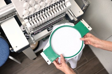 Photo of Woman using embroidery machine to make design on T-shirt indoors, top view