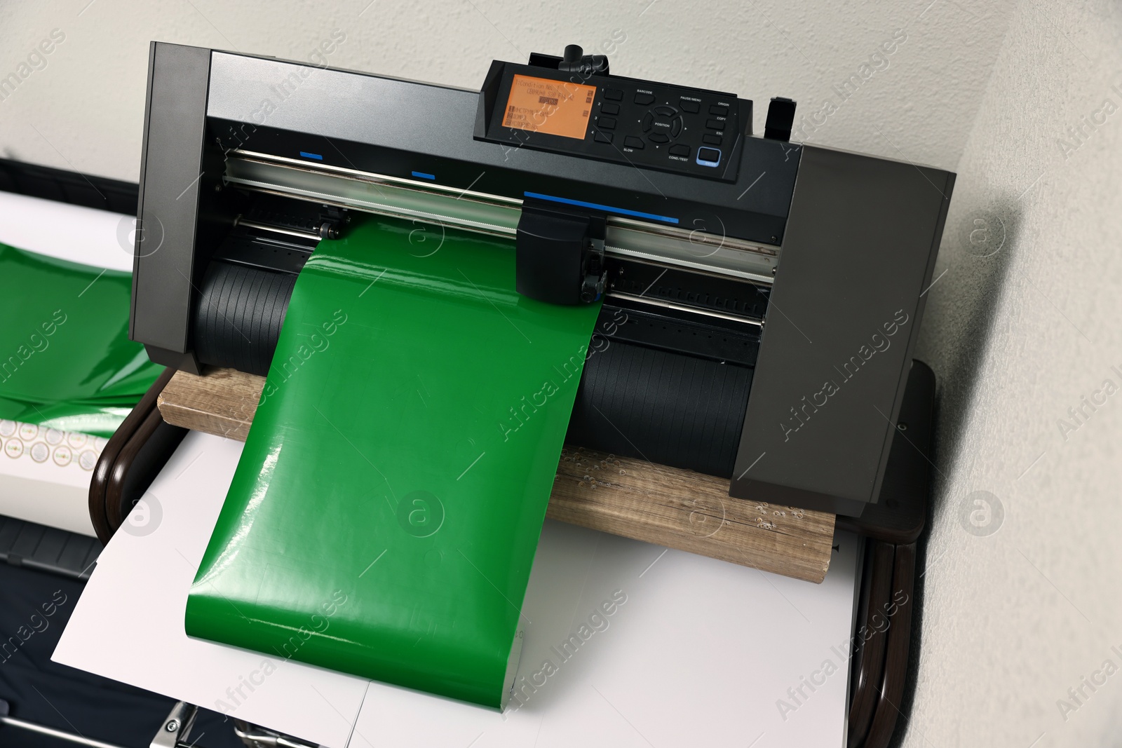 Photo of Modern cutting machine with green vinyl sheet indoors, closeup