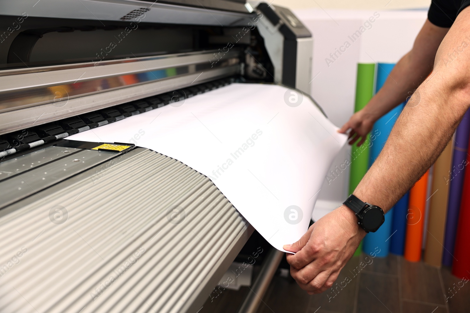 Photo of Man using wide-format printer indoors, closeup. Printing house