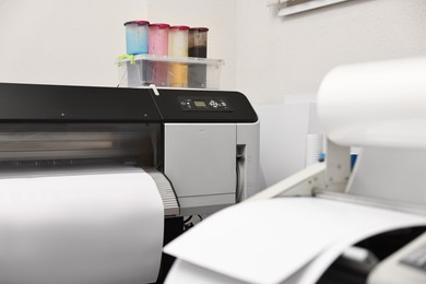 Photo of Wide-format printer and roll laminator with paper indoors, selective focus. Printing house