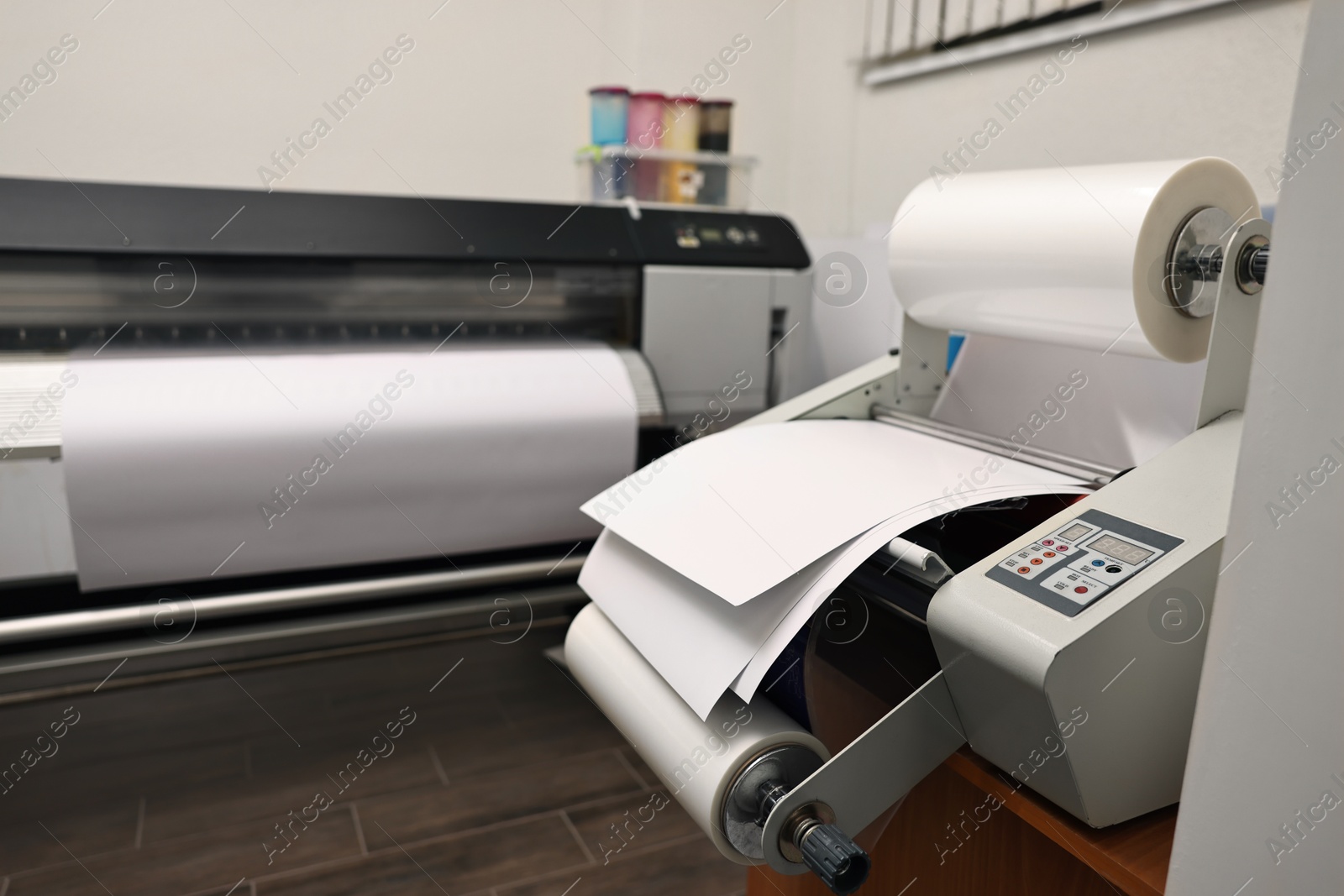 Photo of Modern roll laminator with paper on desk indoors. Printing house