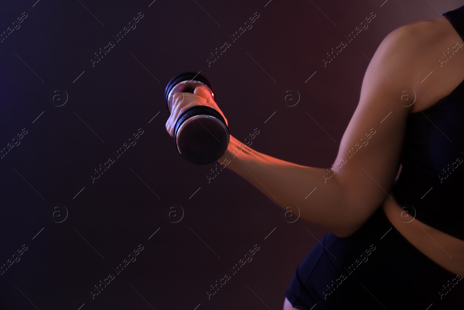 Photo of Woman exercising with dumbbell in smoke on dark background, closeup