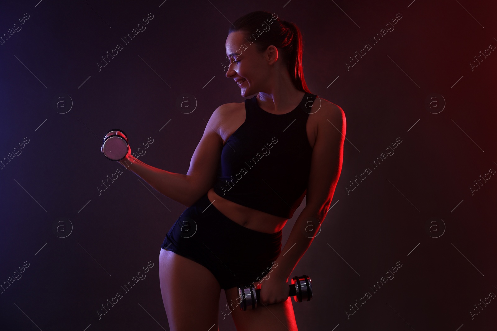 Photo of Woman exercising with dumbbells in smoke on dark background