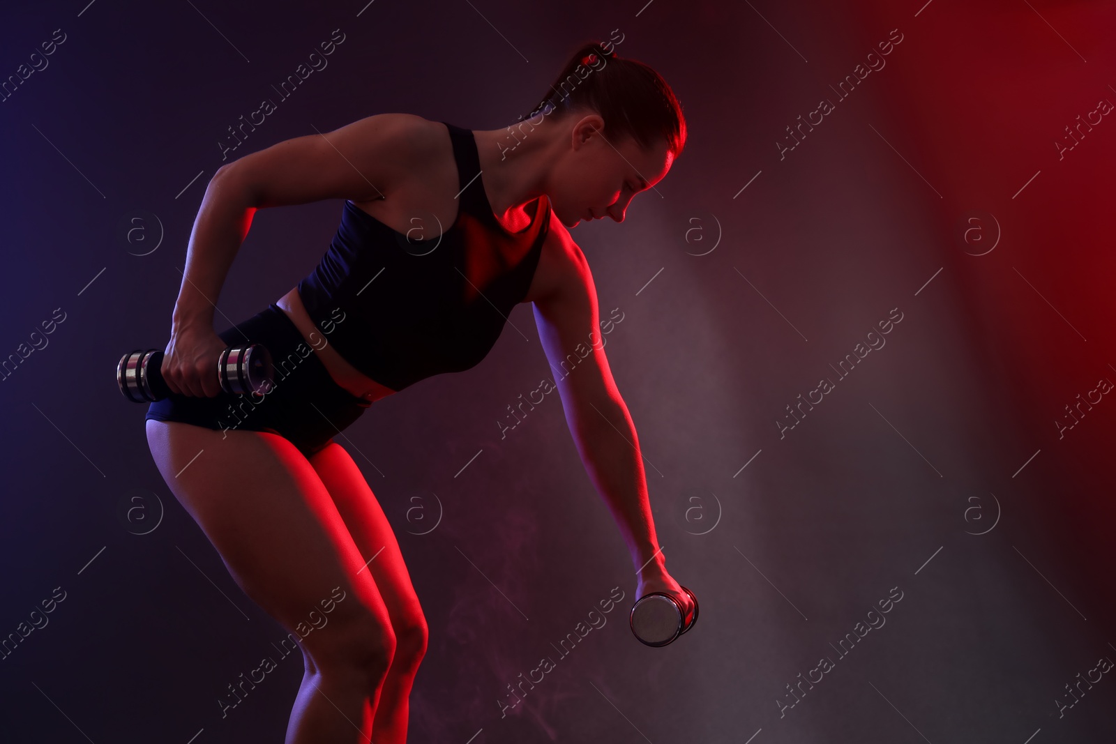 Photo of Woman exercising with dumbbells in smoke on dark background, space for text