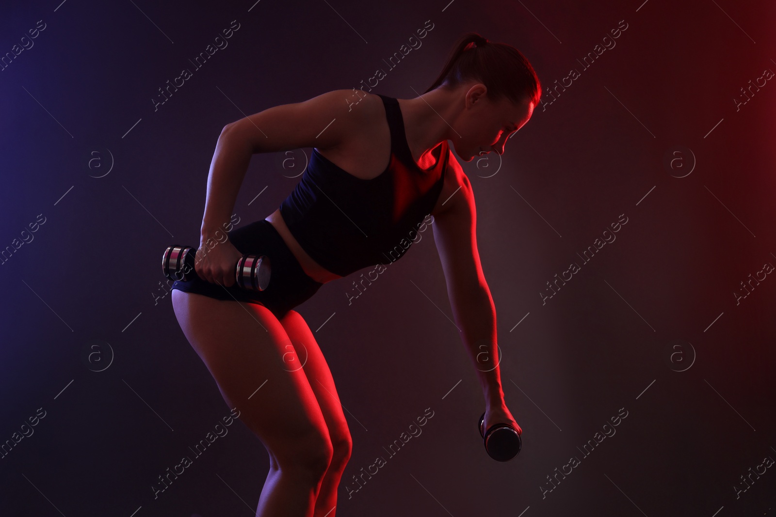 Photo of Woman exercising with dumbbells in smoke on dark background