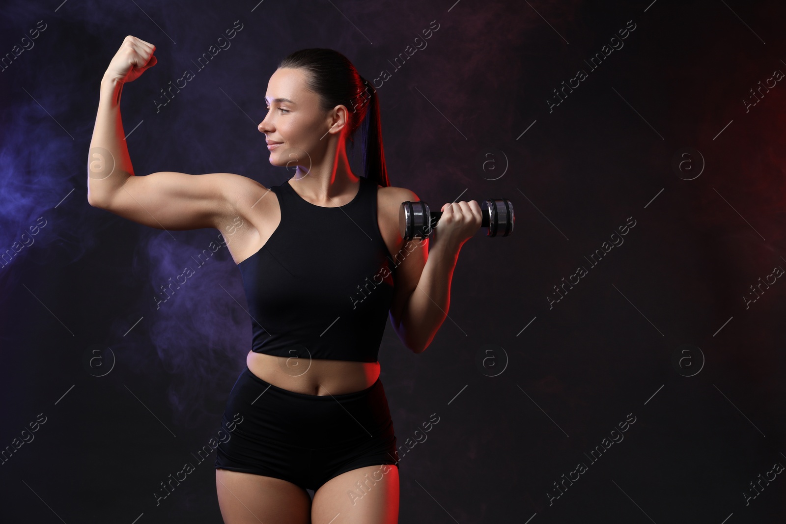 Photo of Woman exercising with dumbbell in smoke on dark background, space for text