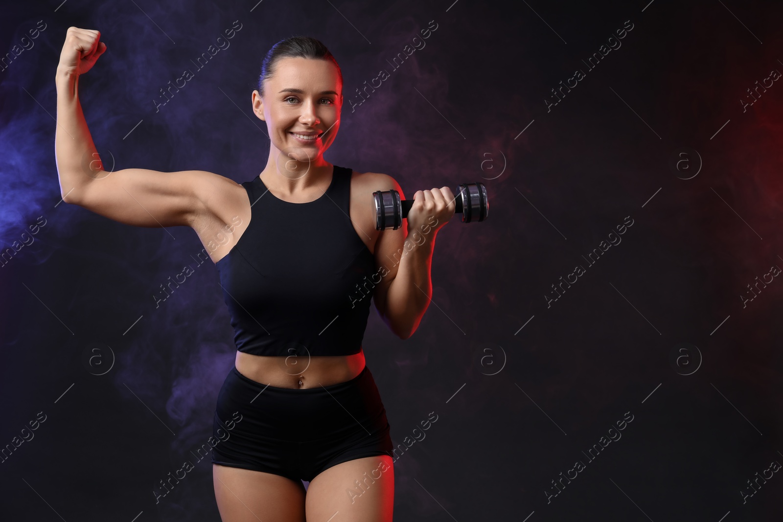 Photo of Woman exercising with dumbbell in smoke on dark background, space for text