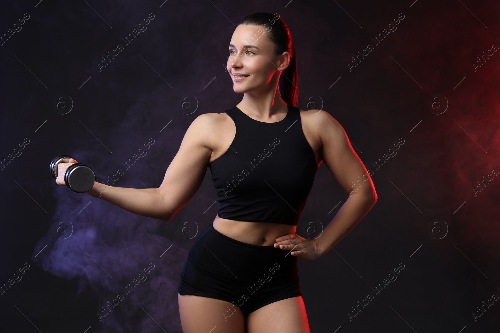 Photo of Woman exercising with dumbbell in smoke on dark background