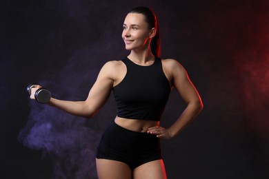 Woman exercising with dumbbell in smoke on dark background