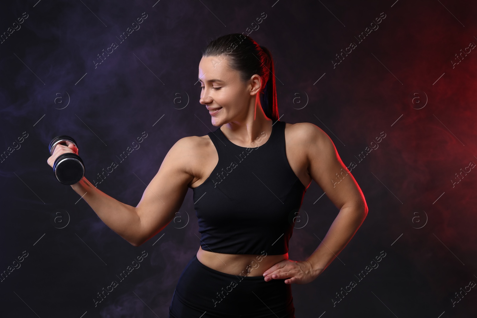 Photo of Woman exercising with dumbbell in smoke on dark background