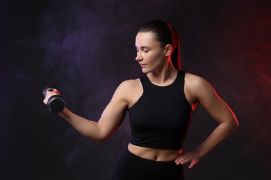 Photo of Woman exercising with dumbbell in smoke on dark background