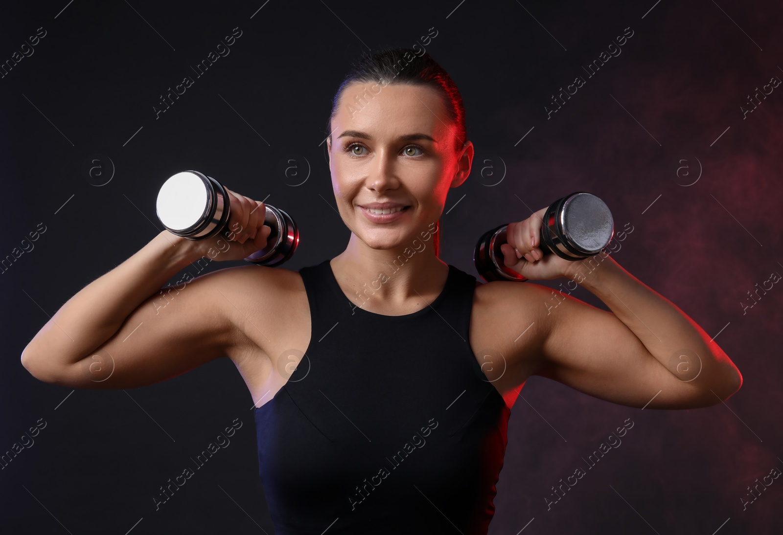 Photo of Woman exercising with dumbbells in smoke on dark background