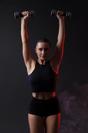 Photo of Woman exercising with dumbbells in smoke on dark background