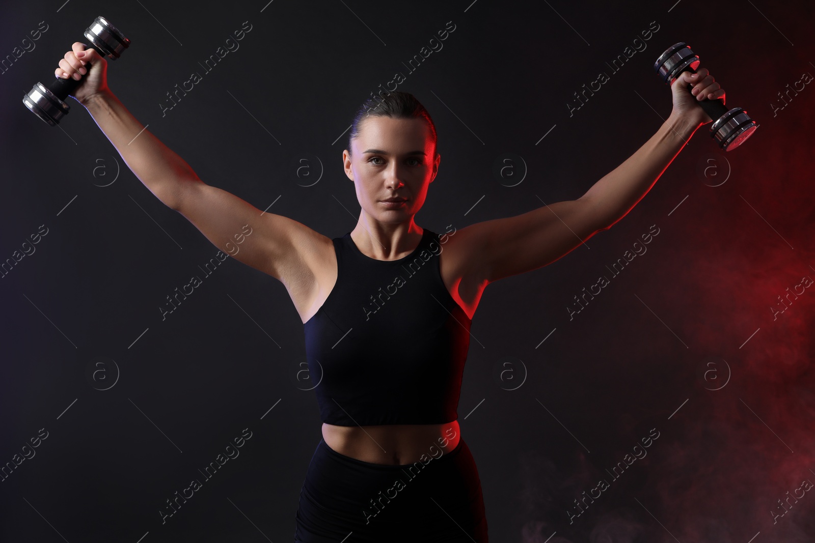 Photo of Woman exercising with dumbbells in smoke on dark background