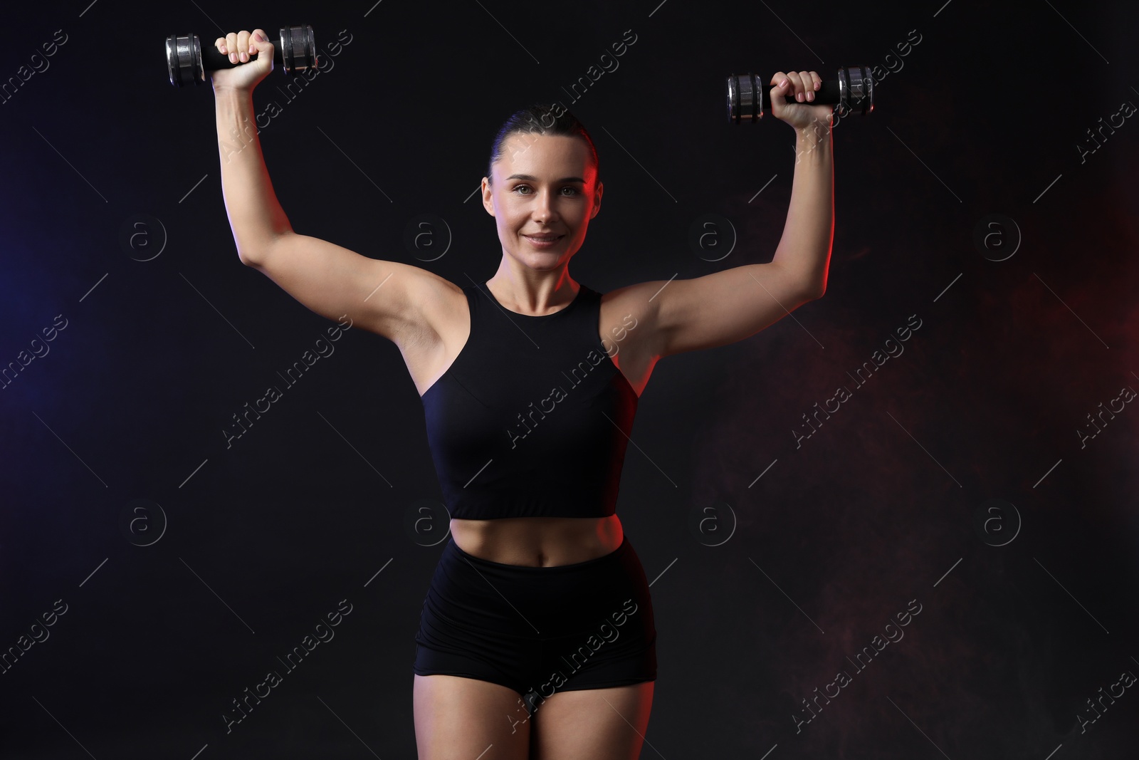 Photo of Woman exercising with dumbbells in smoke on dark background