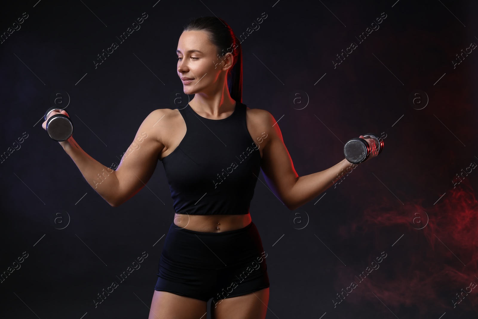 Photo of Woman exercising with dumbbells in smoke on dark background