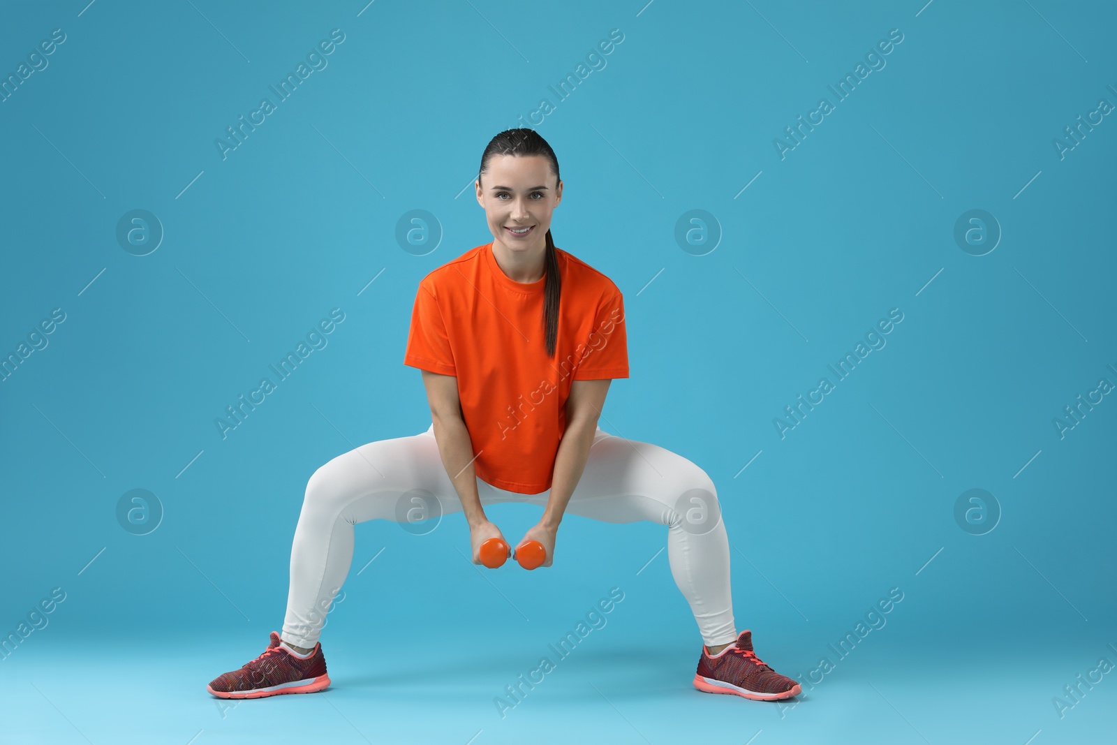 Photo of Woman exercising with dumbbells on light blue background