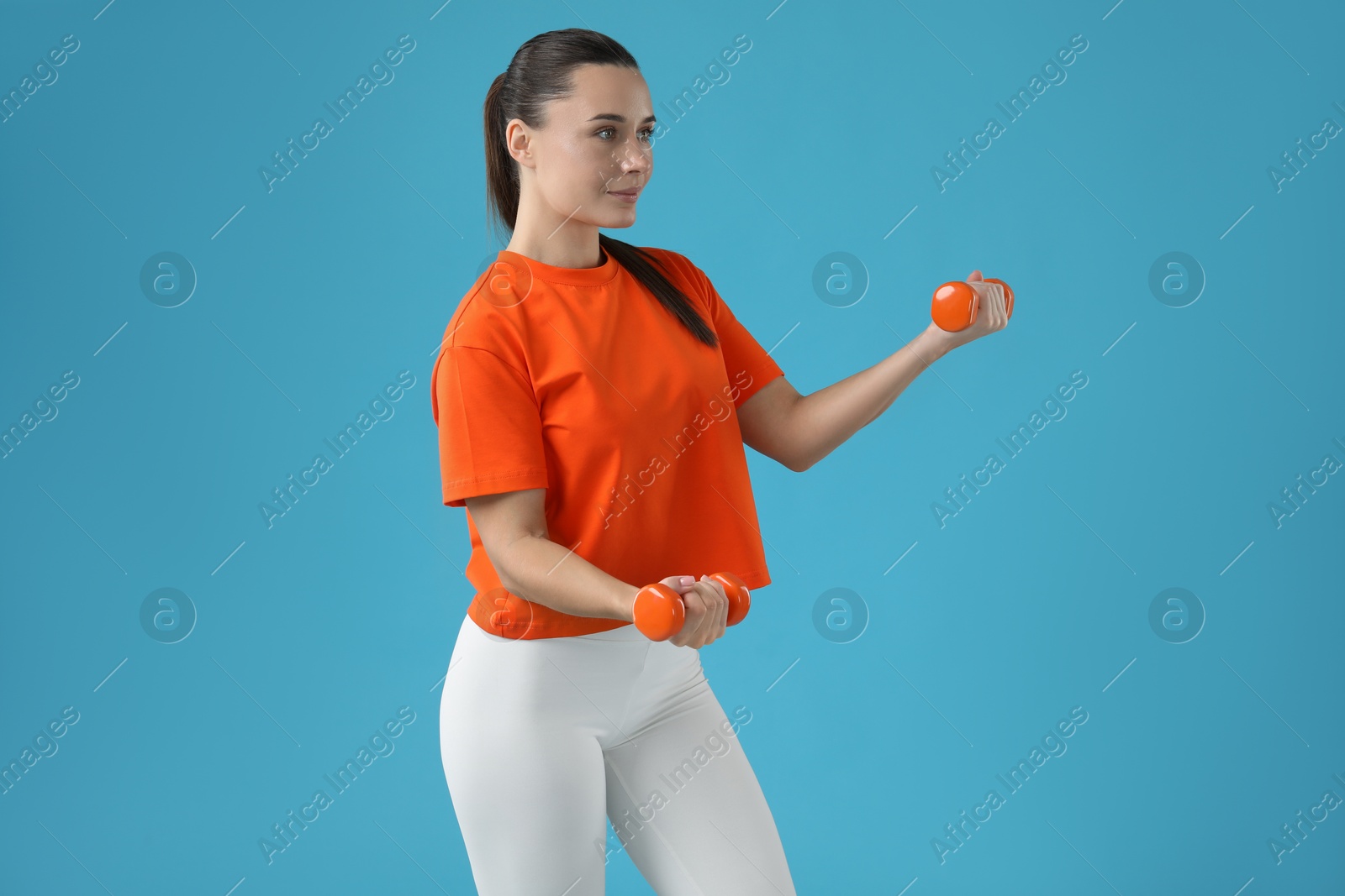 Photo of Woman exercising with dumbbells on light blue background