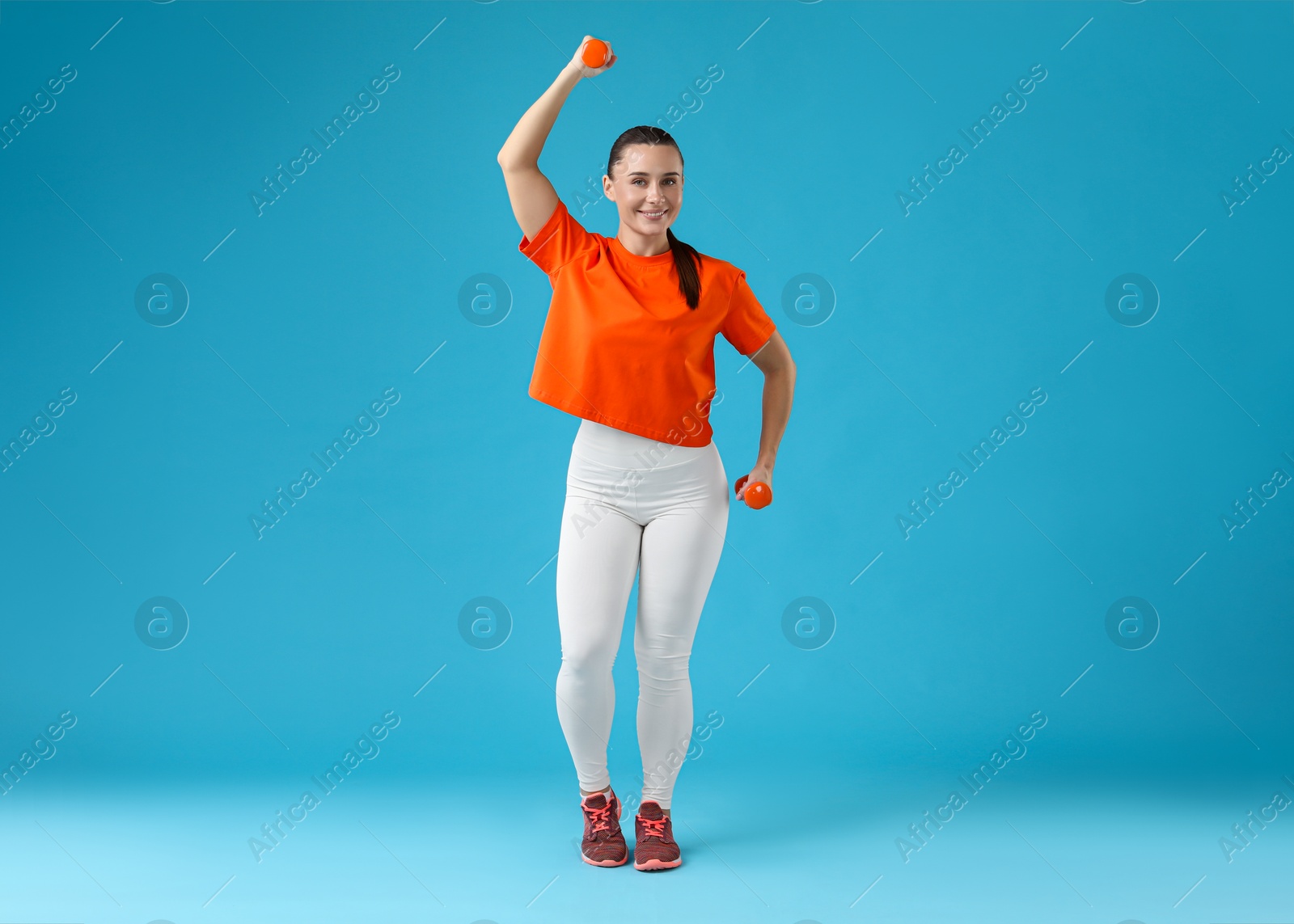 Photo of Woman exercising with dumbbells on light blue background