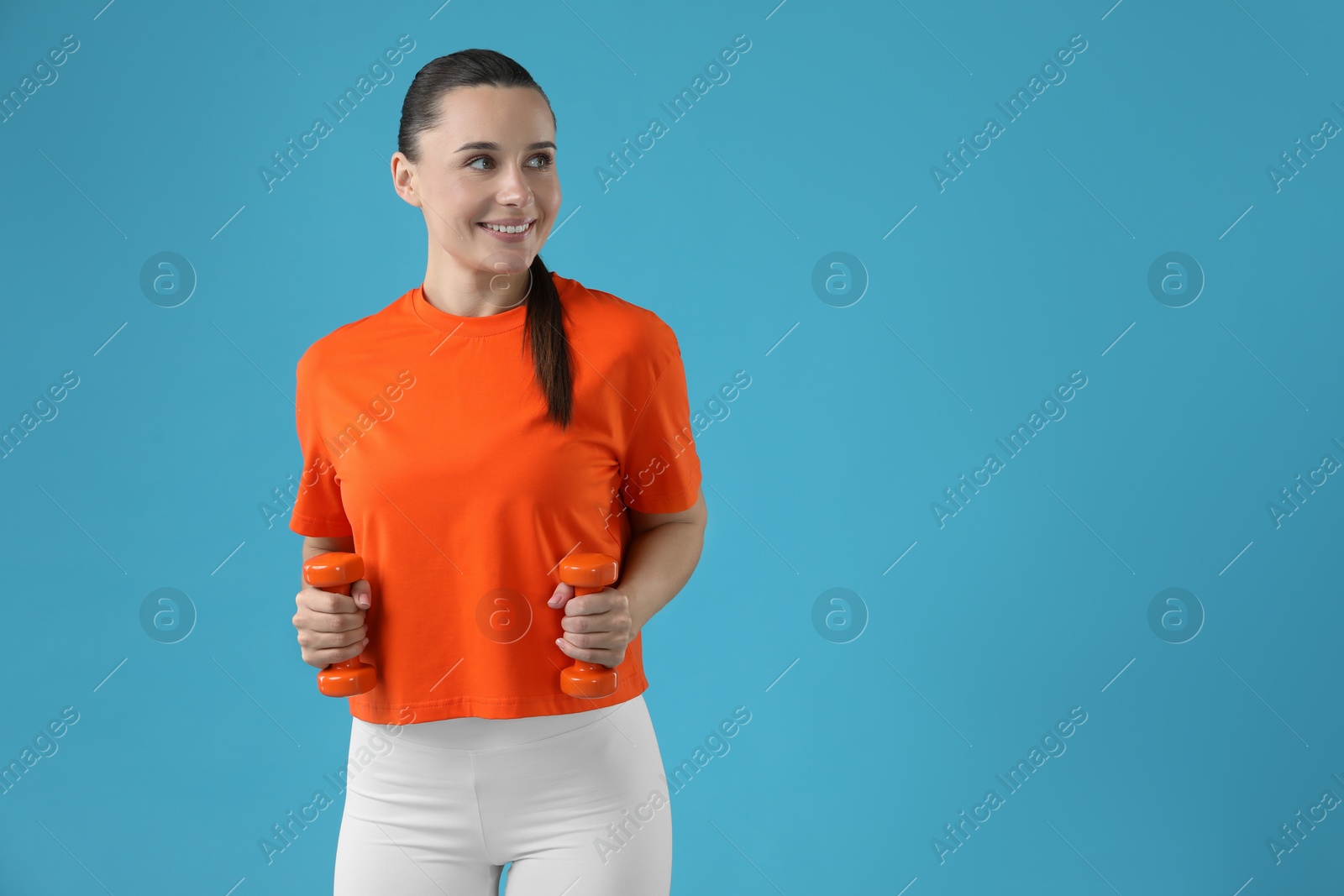 Photo of Woman exercising with dumbbells on light blue background, space for text