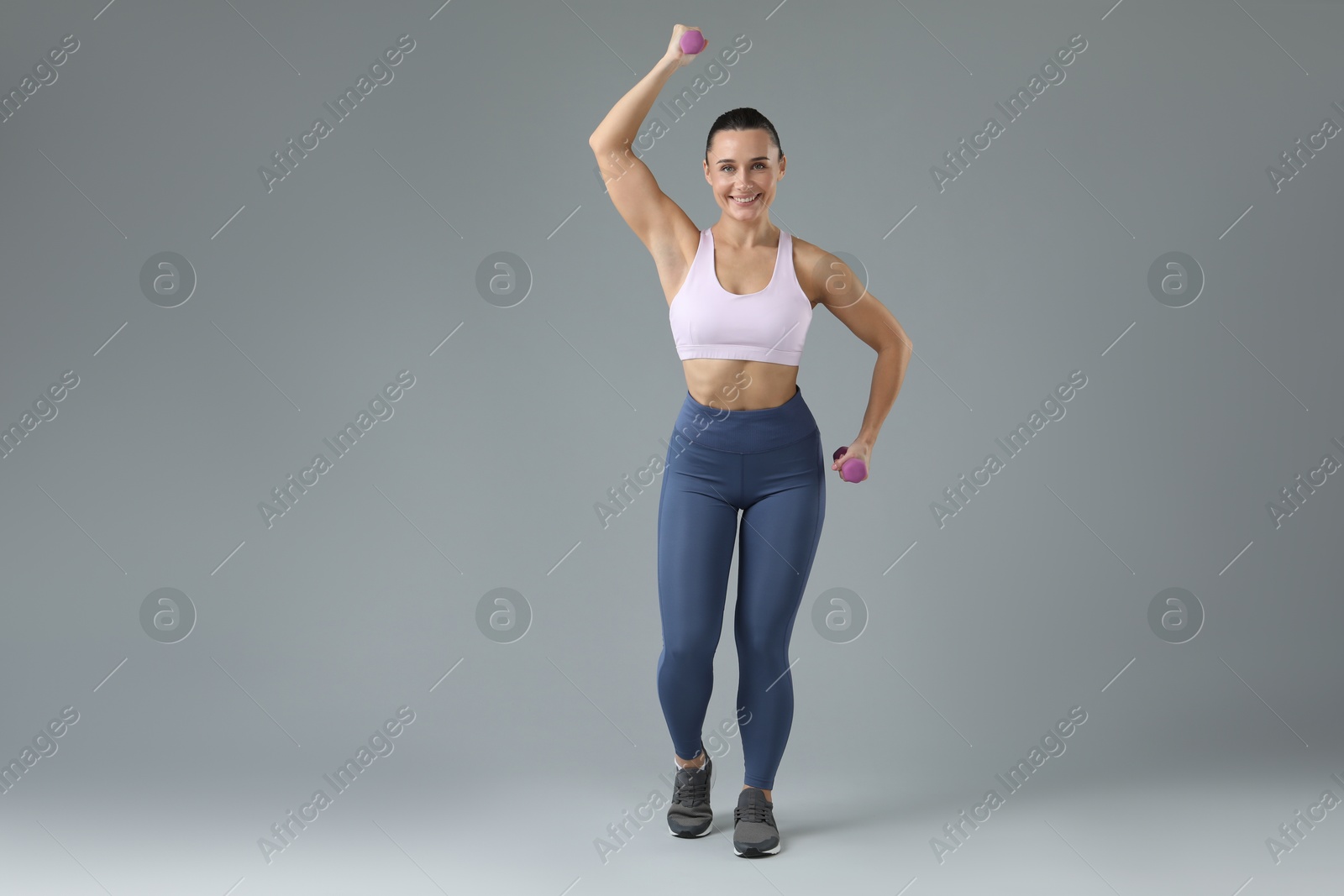 Photo of Woman exercising with dumbbells on light grey background