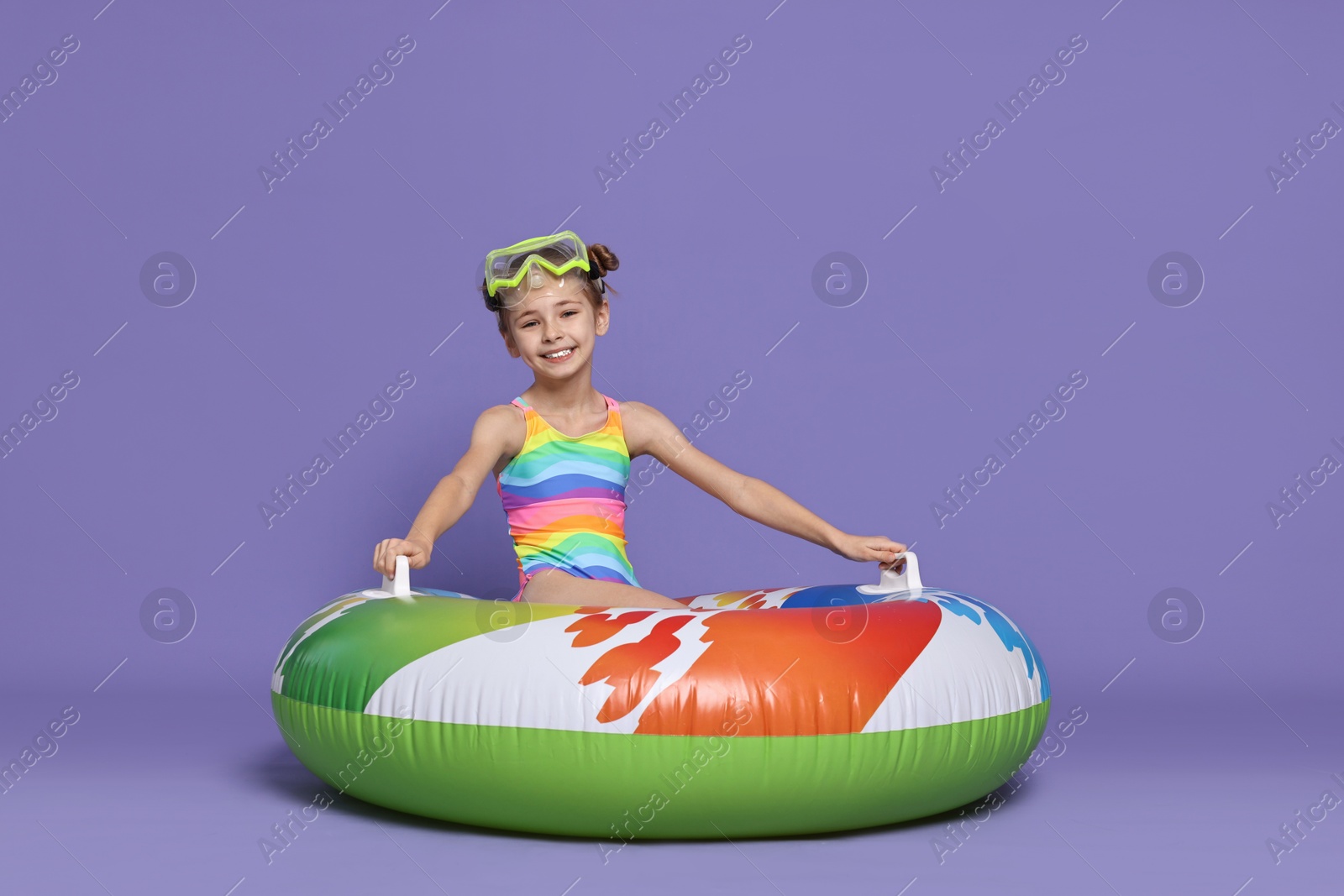 Photo of Happy girl in beachwear with diving mask and inflatable ring on purple background