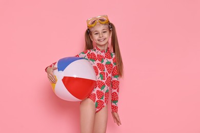 Happy girl in beachwear with diving mask and inflatable ball on pink background