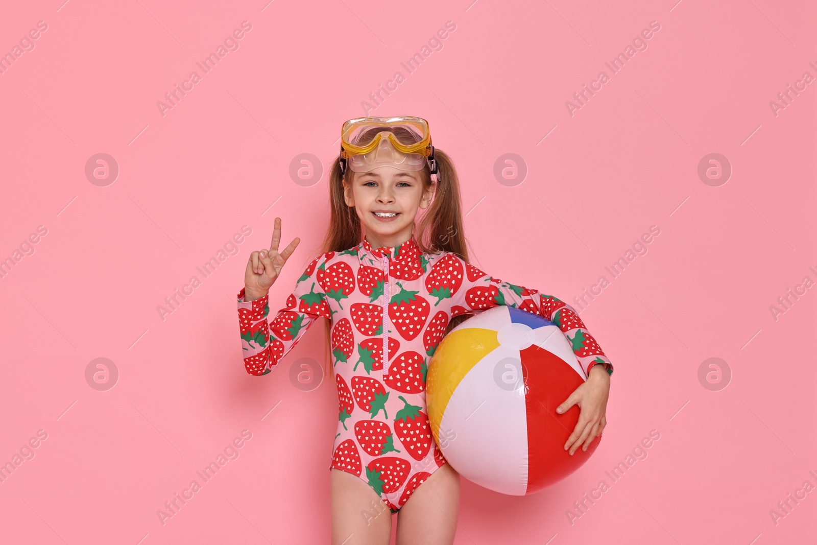 Photo of Happy girl in beachwear with diving mask and inflatable ball on pink background