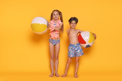 Photo of Happy little kids in beachwear with inflatable balls on orange background