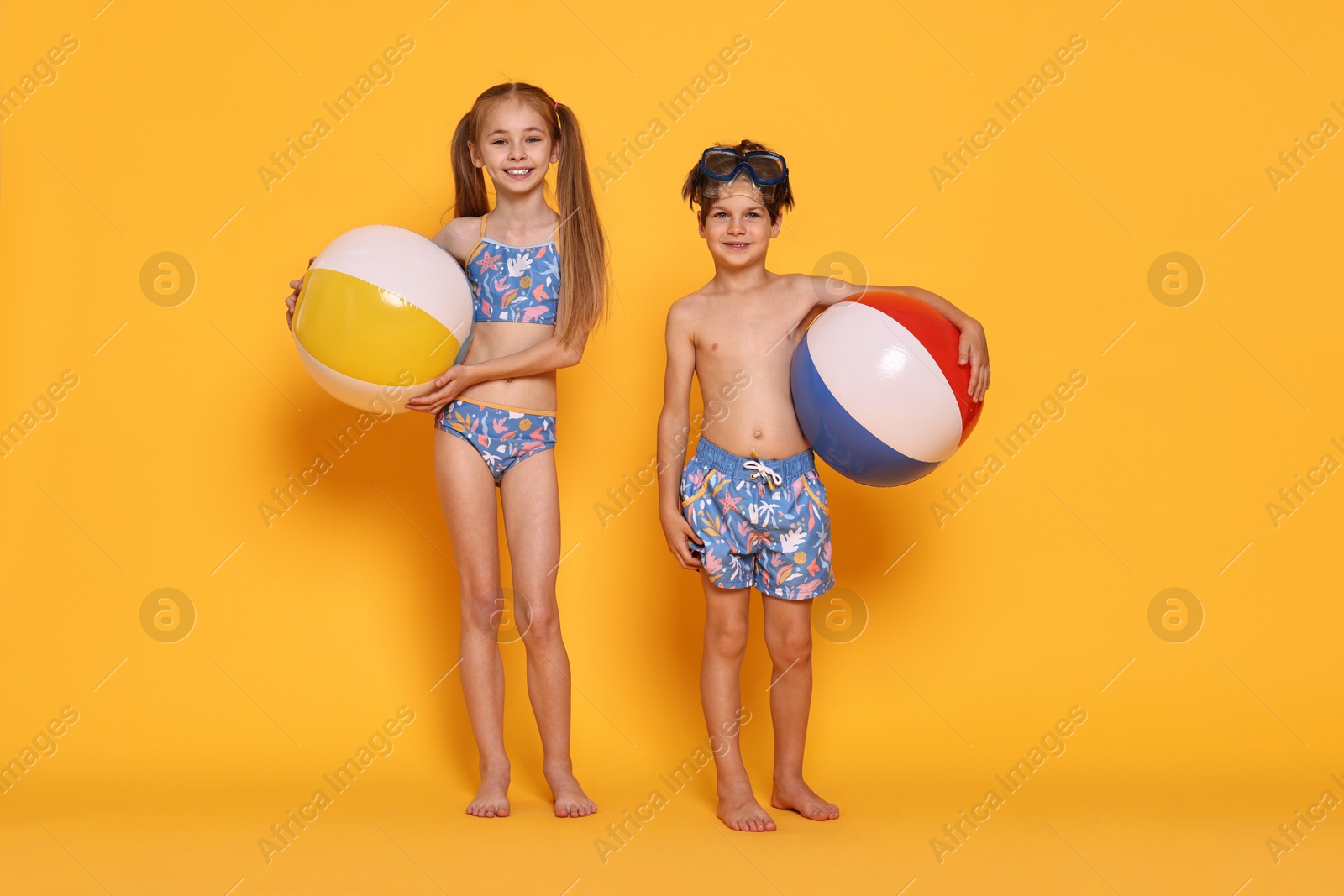 Photo of Happy little kids in beachwear with inflatable balls on orange background