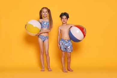 Photo of Happy little kids in beachwear with inflatable balls on orange background