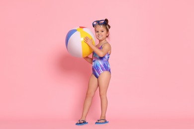 Photo of Cute little girl in swimsuit with inflatable ball on light pink background