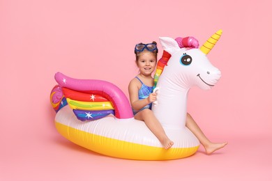 Photo of Cute little girl in swimsuit with unicorn pool float on light pink background