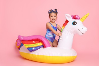 Photo of Cute little girl in swimsuit with unicorn pool float on light pink background