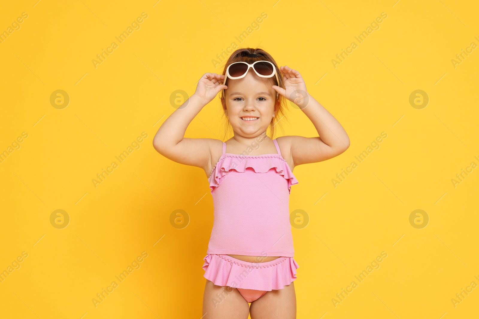 Photo of Cute little girl in swimsuit on orange background