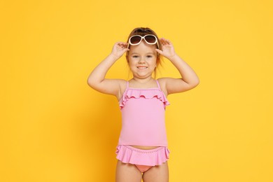 Photo of Cute little girl in swimsuit on orange background