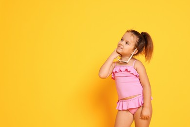 Photo of Cute little girl in swimsuit on orange background. Space for text