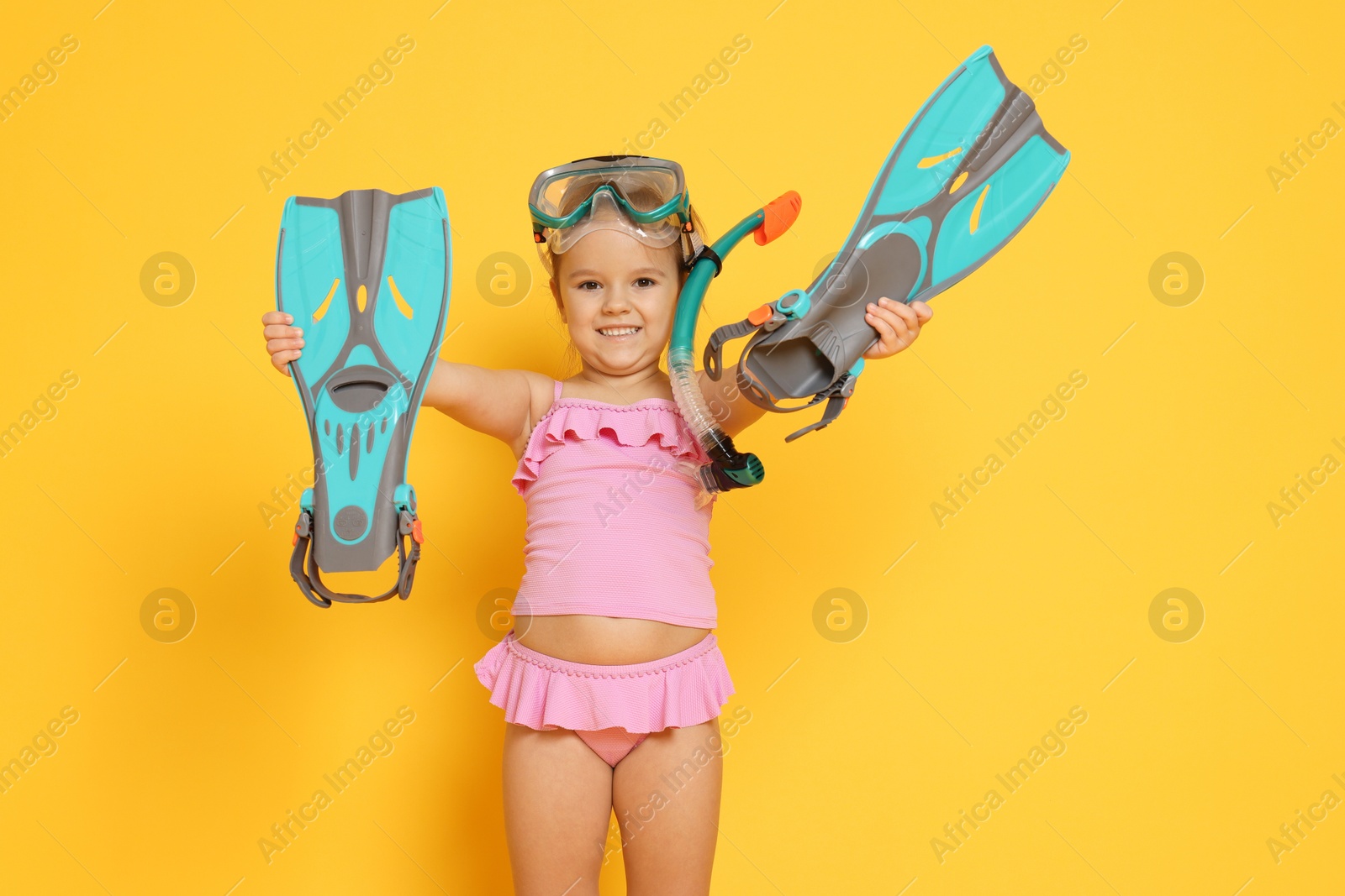 Photo of Cute little girl in swimsuit with snorkeling equipment on orange background