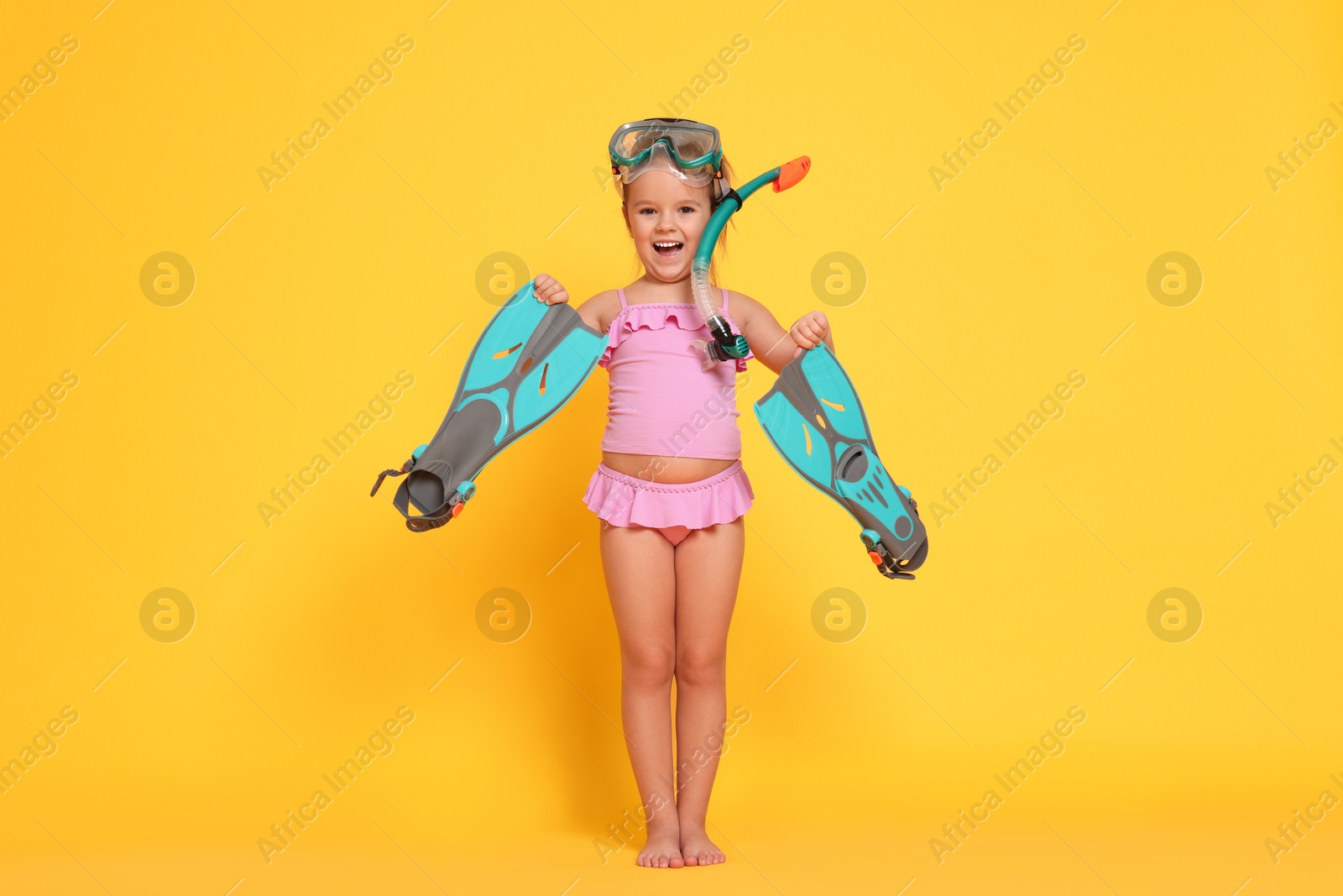 Photo of Cute little girl in swimsuit with snorkeling equipment on orange background