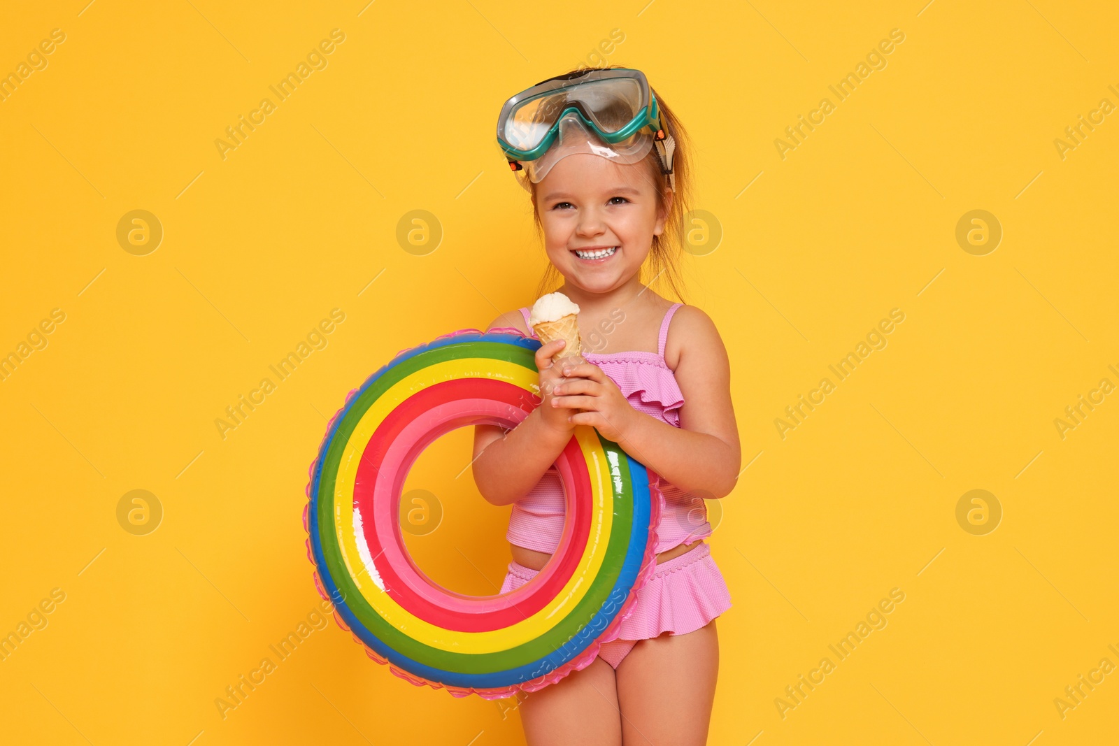 Photo of Cute little girl in swimsuit with inflatable ring eating ice cream on orange background