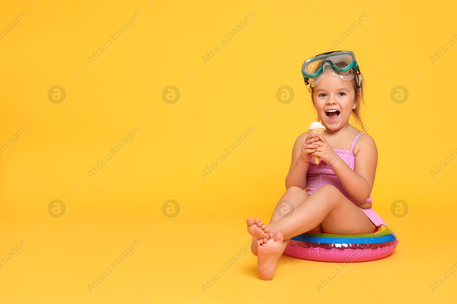 Photo of Cute little girl in swimsuit with inflatable ring eating ice cream on orange background. Space for text