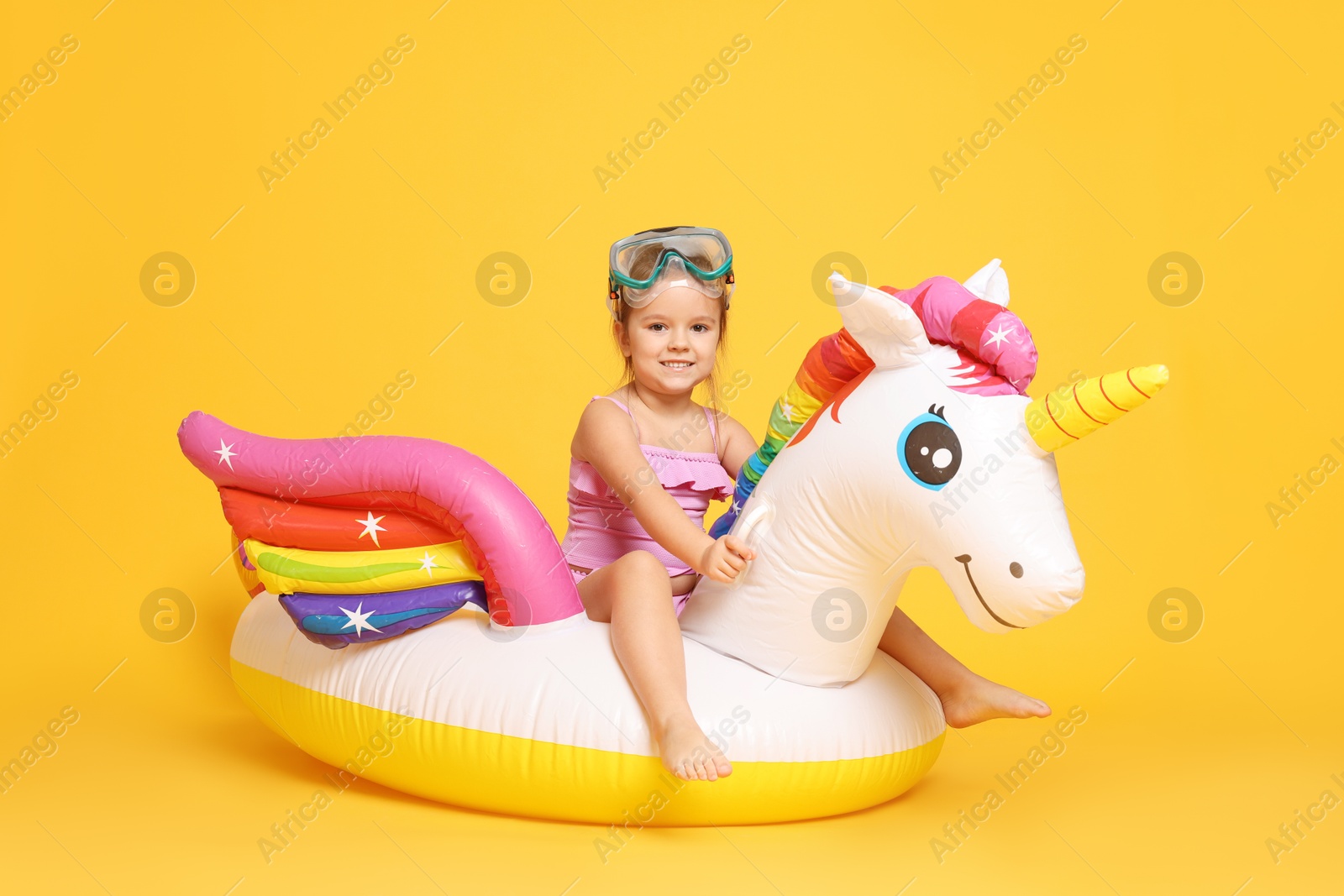 Photo of Cute little girl in swimsuit with unicorn pool float on orange background